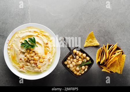 Piatto Lay Hummus in piatto di argilla condito con ceci e foglie di coriandolo verde su tavolo di pietra servito con tortilla patatine Foto Stock