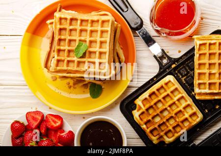 Vista piatta sulle cialde belghe sulla padella colata e. accatastato su un piatto con fragole sciroppate e caffè da parte Foto Stock