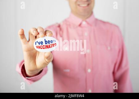 Pin del bottone della campagna di vaccinazione in dita maschio caucasiche. Sono stato vaccinato testo. Foto Stock