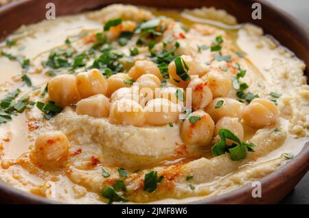 Vista sul closeup all'Hummus sormontato da olio di oliva di fagioli e foglie di coriandolo verde sul tavolo da cucina Foto Stock