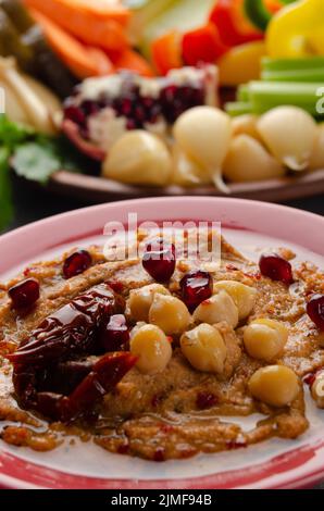 Vista dall'angolo basso sul piatto di hummus vegetale con pomodoro essiccato al sole e ricoperto di ceci e olio d'oliva Foto Stock