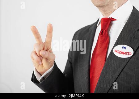 Medio età uomo caucasico in tuta con bottone pin sono vaccinato mostrando V gesto Foto Stock