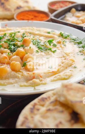 Vista sul closeup all'Hummus sormontato da olio di oliva di fagioli e foglie di coriandolo verde sul tavolo da cucina con pane pita Foto Stock