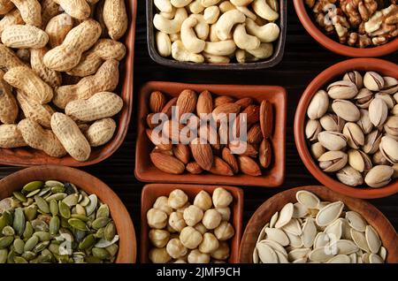 Vista piatta su frutta a guscio e semi assortiti in argilla ciotole su tavolo da cucina in legno Foto Stock