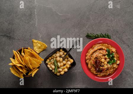 Hummus piatto con pomodori secchi in piatto di argilla con ceci e foglie di coriandolo verde su tavola di pietra servita con Foto Stock