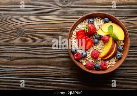 Piatto di laici frutto sano muesli con pesche mandorle di fragola e blackberry in argilla piatto di legno sul tavolo da cucina Foto Stock