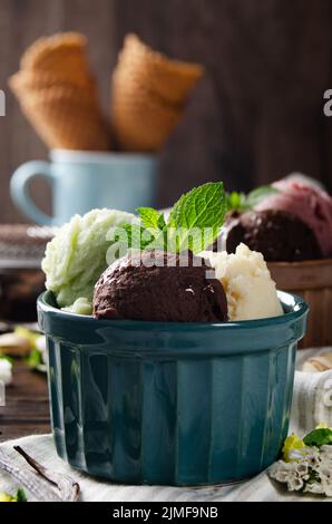 Tre cucchiai di pistacchio di vaniglia e palline di gelato al cioccolato in ciotole di argilla su tavolo da cucina in legno Foto Stock