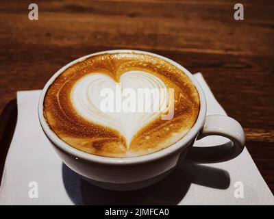 Pausa caffè e concetto di atmosfera romantica. Tazza di cappuccino al caramello con schiuma a forma di cuore realizzata con latte senza lattosio, servita o Foto Stock