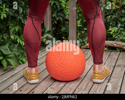 il maschio in pantaloni di compressione sta esercitandosi con una sfera pesante di slam su un ponte del cortile, idoneità funzionale e concetto di gym del cortile Foto Stock