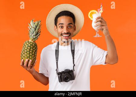 Amichevole afroamericano sorridente uomo sollevare drink come divertirsi, godendo vacanza su isola paradiso all'estero, tenendo Foto Stock