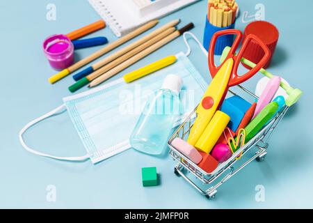 Forniture scolastiche, poppit anti-stress, maschera facciale, bottiglia di igienizzatore, per tornare a scuola su sfondo blu. Covid-19 precauzioni, rimanere in salute. Foto Stock