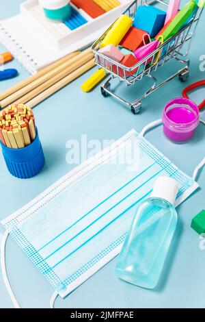 Forniture scolastiche, poppit anti-stress, maschera facciale, bottiglia di igienizzatore, per tornare a scuola su sfondo blu. Covid-19 precauzioni, rimanere in salute. Foto Stock