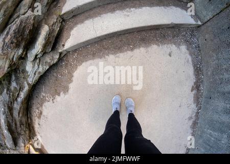 Vista fisheye guardando verso il basso una donna che indossa leggings neri e scarpe comode, mentre su gradini di cemento Foto Stock