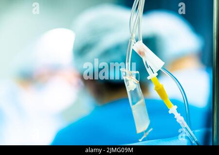 Tubi trasparenti di un contagocce medico con soluzione salina su sfondo sfocato. Foto Stock