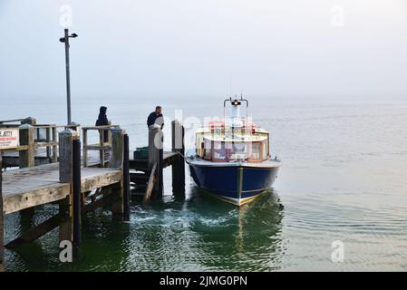 Lo skipper del piccolo traghetto passeggeri Brownsea Enterprise si lega al molo di The Haven, Poole, per consentire a due passeggeri di salire a bordo in un nebbiosa maggio Foto Stock