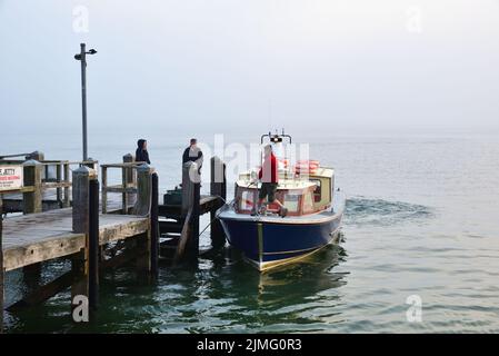 Lo skipper del piccolo traghetto passeggeri Brownsea Enterprise si lega al molo di The Haven, Poole, per consentire a due passeggeri di salire a bordo in un nebbiosa maggio Foto Stock