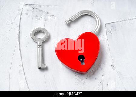 Apri il lucchetto rosso a forma di cuore con una chiave in argento su sfondo di cemento. Romantico concetto di San Valentino. Foto Stock