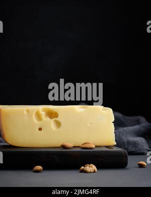 Pezzo triangolare di formaggio maasdam su un pannello di legno marrone Foto Stock