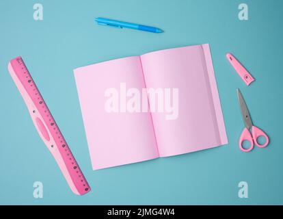 Aprire il notebook con fogli rosa vuoti, forbici e righello su sfondo blu, vista dall'alto Foto Stock