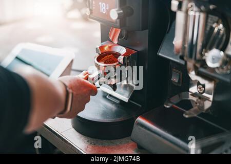 Il barista macina i chicchi di caffè versando in un portafiltro utilizzando una macchina da caffè Foto Stock