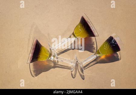 3 bicchieri di cristallo con gelatina di frutta bicolore giacciono su sfondo beige, vista dall'alto. Sole luminoso, ombre interessanti. Vacanza e divertimento atmosfera. Delicio Foto Stock