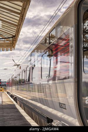 Un carro ferroviario poggia accanto a una piattaforma mentre si prepara a partire. Una tettoia storica è sovratesta e un indicatore luminoso è in distanza. Foto Stock