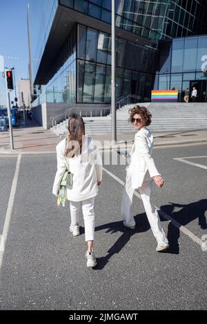 Due donne in abiti alla moda che camminano fuori sullo sfondo di un edificio moderno Foto Stock