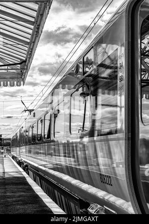 Un carro ferroviario poggia accanto a una piattaforma mentre si prepara a partire. Una tettoia storica è sovratesta e un indicatore luminoso è in distanza. Foto Stock