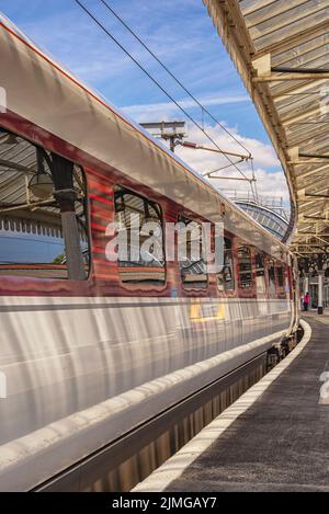 Un carro ferroviario poggia accanto a una piattaforma mentre si prepara a partire. Un baldacchino storico è in testa e ci sono riflessi sulla superficie e il vento Foto Stock