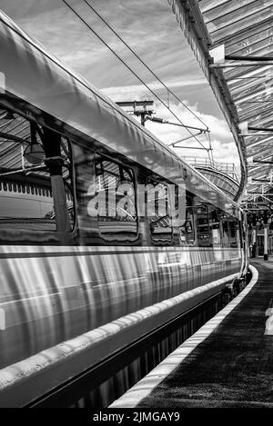 Un carro ferroviario poggia accanto a una piattaforma mentre si prepara a partire. Un baldacchino storico è in testa e ci sono riflessi sulla superficie e il vento Foto Stock