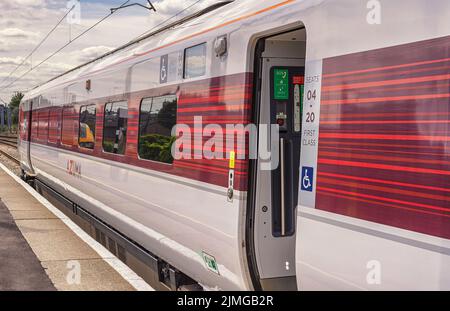 Un carro ferroviario poggia accanto a una piattaforma mentre si prepara a partire. Una porta aperta è in primo piano e un cielo nuvoloso è sopra. Foto Stock