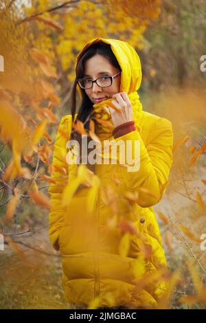 Bella donna in una giacca gialla e sciarpa su uno sfondo autunno foresta Foto Stock