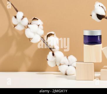 Prodotti cosmetici in vaso di vetro blu con coperchio grigio su un podio in legno a cubetti. Vuoto per marcare a caldo i prodotti, umido Foto Stock