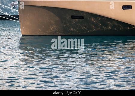 Il riflesso ipnotizzante dell'acqua sul lato lucido di un enorme yacht ancorato, dettagli cromati Foto Stock