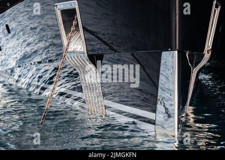 Il riflesso ipnotico dell'acqua sul lato lucido di un enorme yacht ancorato, dettagli cromati, catene e corde alla mur Foto Stock