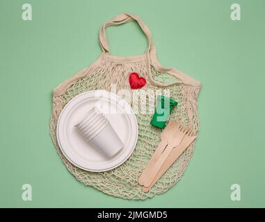 Sacchetto di cotone bianco, vasetti di carta e forchette e cucchiai di legno su sfondo verde. Rifiuti riciclabili, vista dall'alto Foto Stock