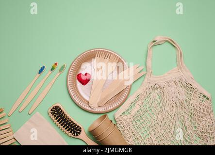 Sacchetto di cotone bianco tessuto, tazzine di carta e spazzolini da denti in legno su sfondo verde. Rifiuti riciclabili, vista dall'alto Foto Stock