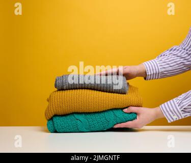 Una donna tiene una pila di cose piegate lavate su uno sfondo giallo. Lavoro di routine a casa Foto Stock