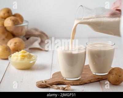 Latte di patate versato in vetro su bg di legno bianco Foto Stock