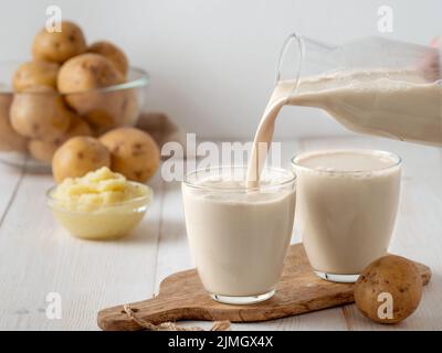 Latte di patate versato in vetro su bg di legno bianco Foto Stock