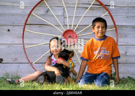 Due bambini nativi americani giocano insieme con un cucciolo. Fort Hall, Idaho Foto Stock