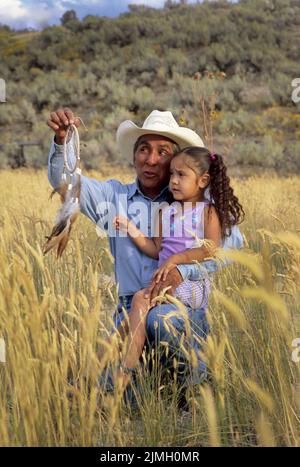 Famiglia nativa americana di un nonno con sua nipote seduta sul ginocchio in un campo mentre racconta la storia del dreamcatcher Foto Stock