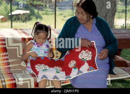 La famiglia nativa americana di una grande nonna, ben nota per il suo beadwork da collezione, mostra a sua grande nipote i vari disegni utilizzati. Handin Foto Stock