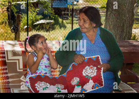 Nonna nativa americana mostra il suo tradizionale beadwork a nonna condividendo una storia sui vari disegni utilizzati. Handin Foto Stock