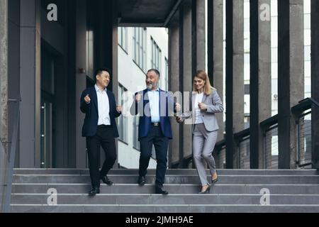 diversi team aziendali, uomo e donna che camminano insieme fuori dall'edificio degli uffici, soddisfatti della vittoria festeggiando, uomini d'affari che ballano sulle scale e sorridenti felici Foto Stock