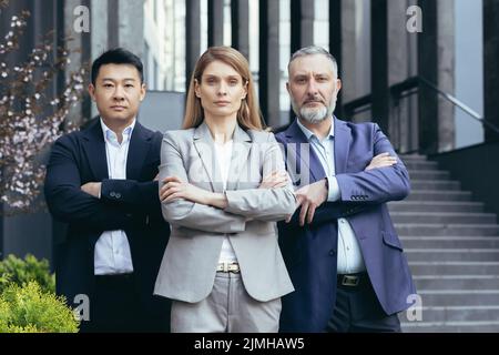 Boss femminile serio e fiducioso con team di lavoratori, gruppo di uomini d'affari al di fuori degli uffici in piedi e guardando la macchina fotografica in concentrazione e pensieroso con le braccia incrociate Foto Stock