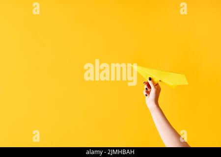 La mano di una donna tiene l'aeroplano di carta su sfondo giallo Foto Stock