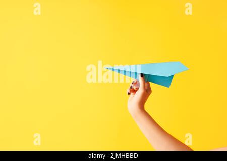 La mano di una donna tiene un aeroplano di carta blu su sfondo giallo Foto Stock