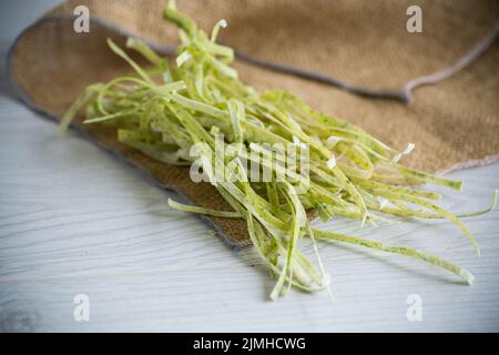 spaghetti crudi verdi fatti in casa essiccati con erbe aromatiche su un tavolo di legno Foto Stock