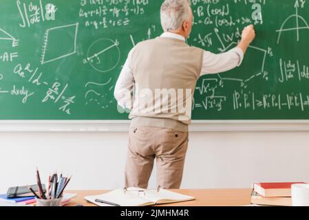 Insegnante di matematica anziano che scrive equazione lavagna Foto Stock